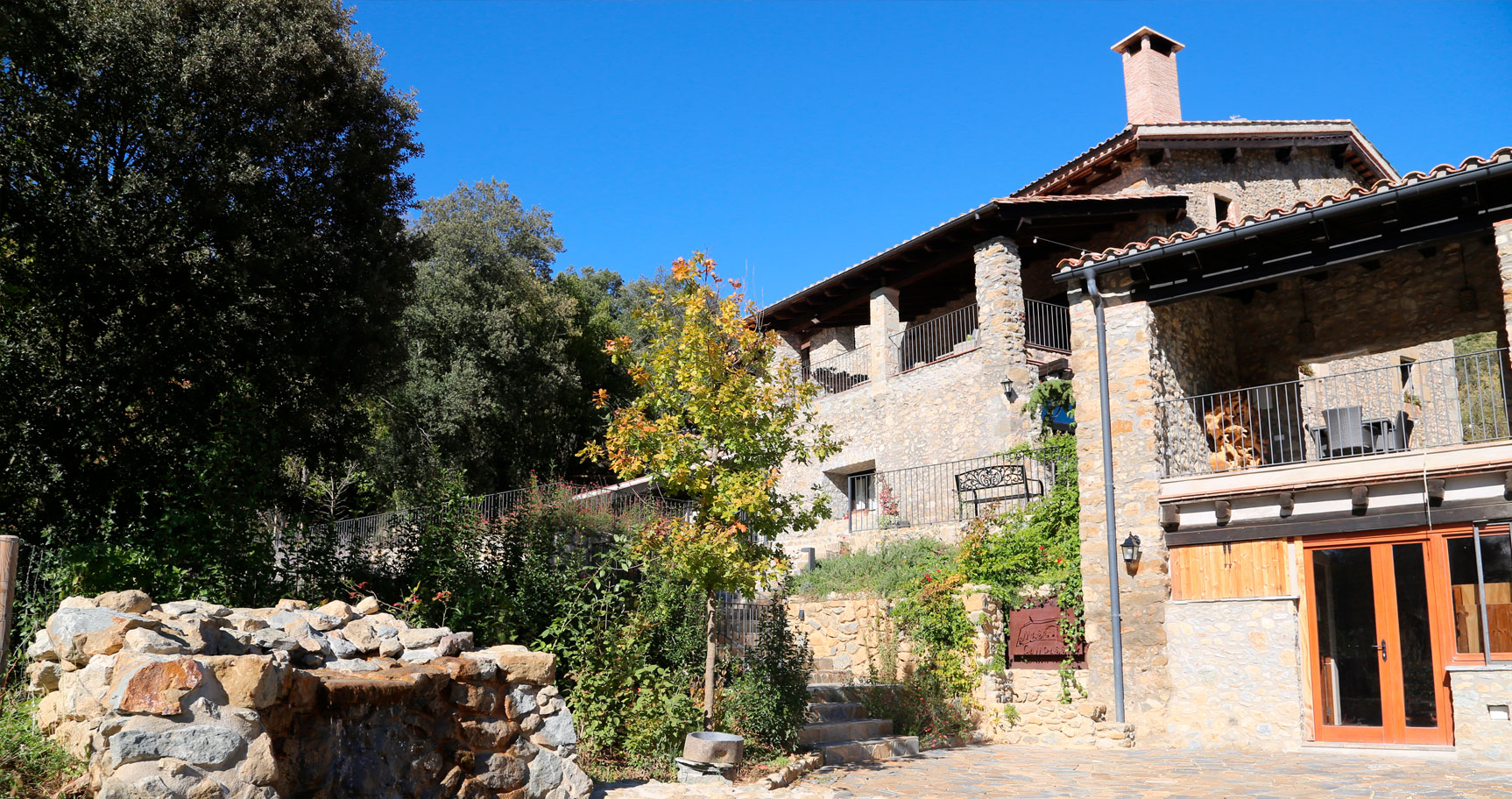 Fachada de piedra de Mas Campassol con terraza, balcones de madera y una fuente de piedra