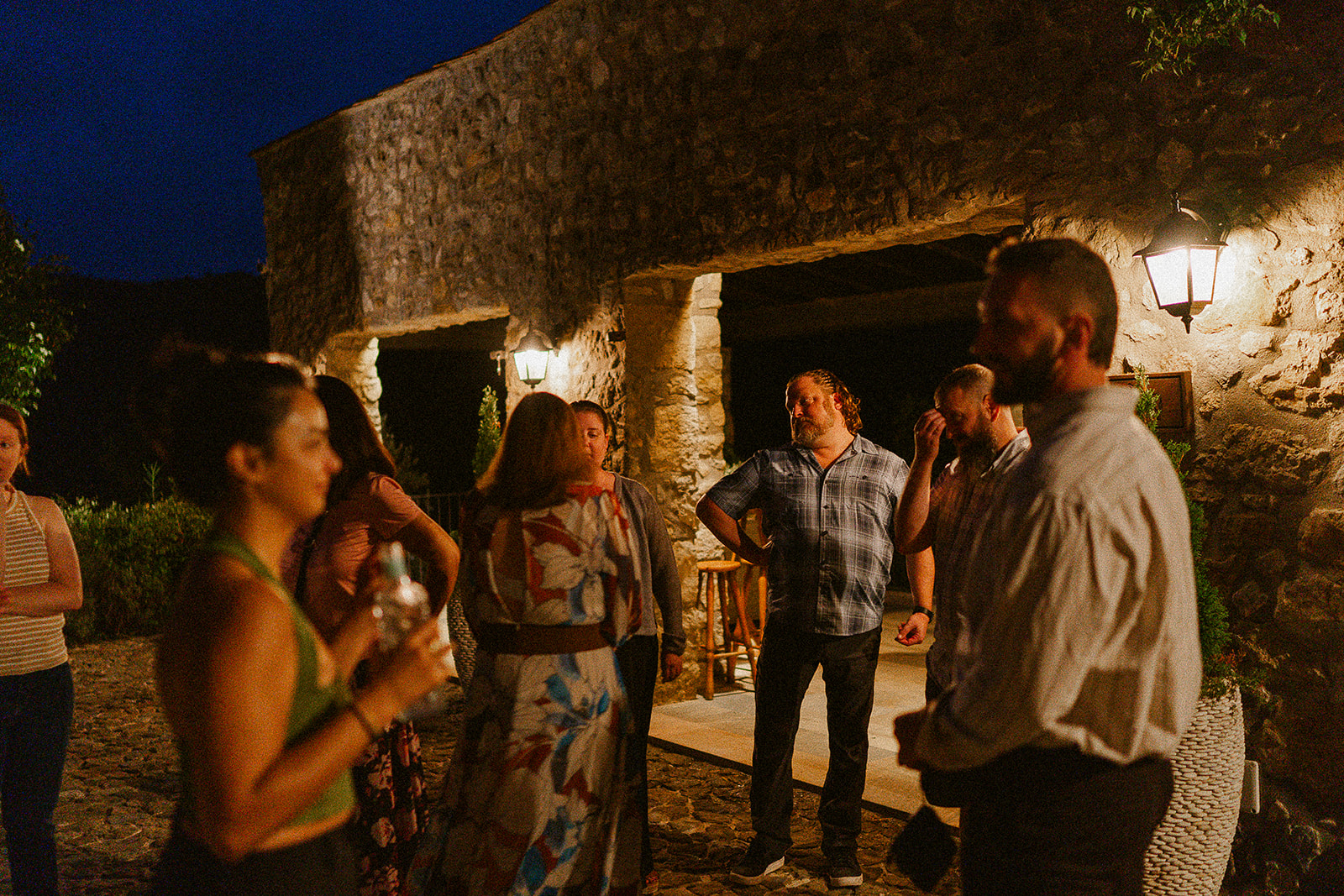 Invitados disfrutando el cóctel nocturno en los arcos de piedra iluminados de Mas Campassol, boda en La Garrotxa